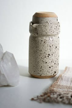 a white and brown jar sitting on top of a table next to a piece of cloth