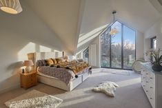 a bedroom with a bed, dresser and large windows