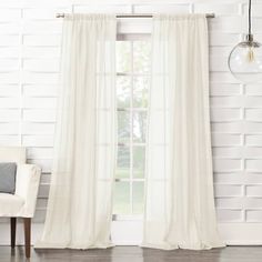 a white curtain hanging from a window next to a chair