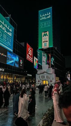 many people are walking around in the middle of an outdoor plaza at night with large billboards above them