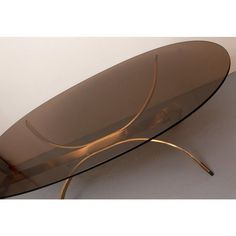 an oval glass table with metal legs and a curved design on the top, against a white wall