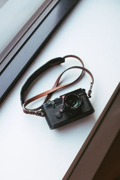 a camera sitting on top of a window sill next to a brown strap that is attached to it