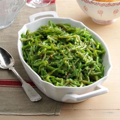 a white bowl filled with green beans on top of a table next to a silver spoon