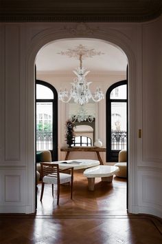 an open door leading to a living room with chandelier and chairs in it