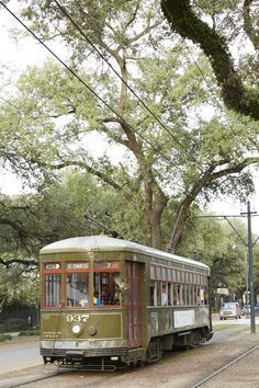 an old fashioned trolley car is on the tracks in front of a large oak tree