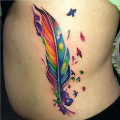 a colorful feather tattoo on the side of a woman's stomach, with butterflies around it