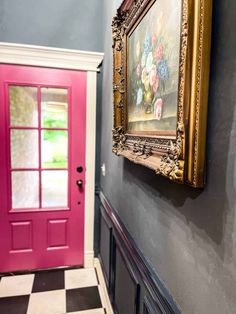 a painting hangs on the wall next to a pink door and black and white checkered floor