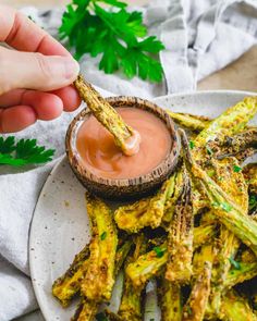 a person dipping sauce on top of some asparagus fries with parsley in the background