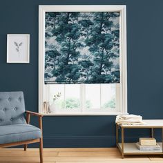 a living room with blue walls and a window covered in tree print roman shades on the windowsill