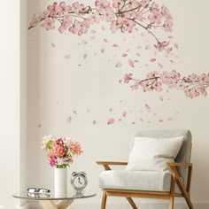 a white chair sitting in front of a wall with pink flowers on it and a vase