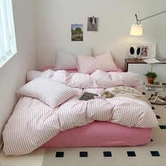 a bed with pink and white striped sheets in a room next to a lamp on a table