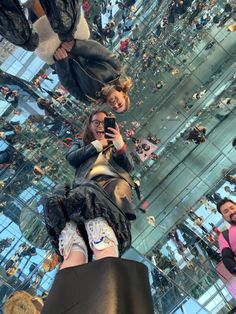 two women taking pictures with their cell phones in front of a mirrored wall filled with people