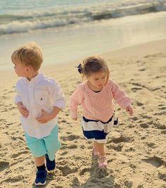 two young children are walking on the beach