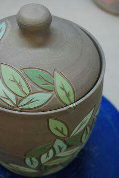 a pot with leaves painted on it sitting on top of a blue plate next to a cup