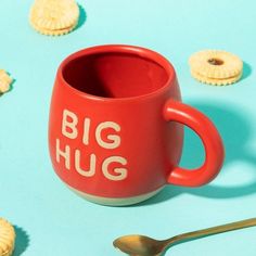 a red mug with the words big hug on it next to some cookies and spoon