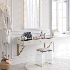 a white vanity with lights on the wall and a stool in front of it next to a mirror