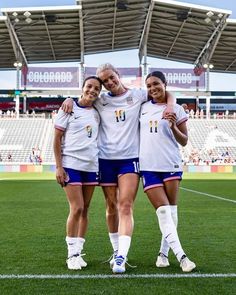 three girls are standing together on the soccer field