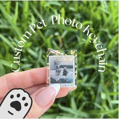 a hand holding a tiny photo with a dog's paw on it in front of some grass