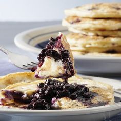 a plate with pancakes and blueberry sauce being drizzled onto it by a fork