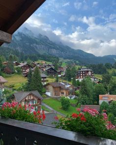 a view of some houses in the mountains from a balcony with flowers and bushes on it