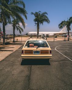 an old car parked on the tarmac in front of palm trees and a plane