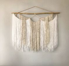 macrame wall hangings with white yarn and wood sticks on the top, in front of a white wall