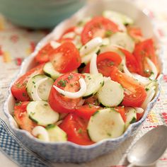 a bowl filled with cucumbers and tomatoes on top of a table next to a spoon