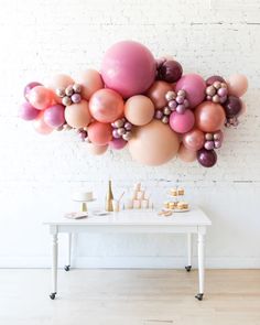 a white table topped with lots of pink and gold balloons next to a wall mounted balloon art