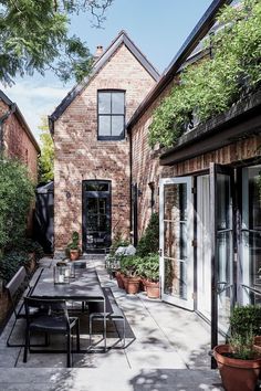 an outdoor dining table and chairs in front of a brick house with potted plants