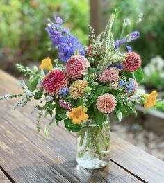 a vase filled with lots of different colored flowers on top of a wooden table next to plants