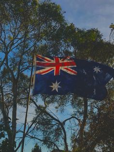 an australian flag is flying in the air next to trees and blue sky with white clouds