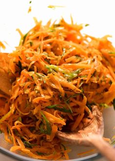 shredded carrots and green onions on a plate with a wooden spoon in it, ready to be eaten