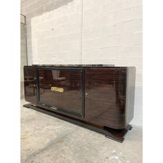 an art deco sideboard with glass doors and brass hardware on the bottom, in front of a white brick wall