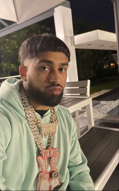 a man with a beard wearing a hoodie and necklaces sitting on a bench