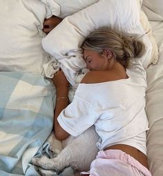 a woman laying in bed with her dog sleeping next to her on top of the pillow