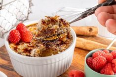 a person is cutting up some food in a bowl with raspberries on the side