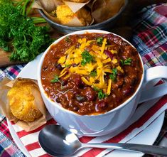 a white bowl filled with chili and cheese on top of a red and white napkin