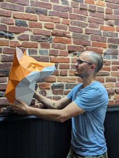 a man is holding an origami fox head in front of a brick wall