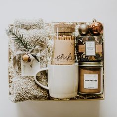 a gift box filled with candles, coffee mug and other holiday items on a blanket