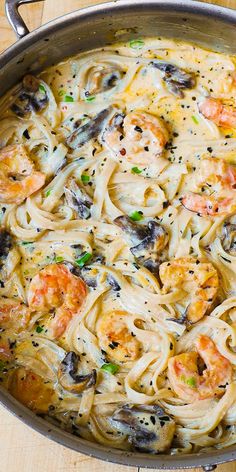 a pan filled with pasta and shrimp on top of a wooden table