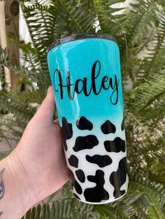 a hand holding up a blue and black tumbler with the word taley painted on it