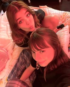 two young women laying on top of a bed next to each other with one pointing at the camera