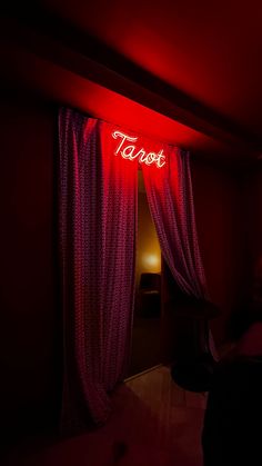 a red neon sign hanging from the side of a wall next to a bed in a dark room