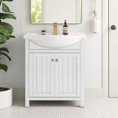 a white sink sitting under a mirror next to a potted plant