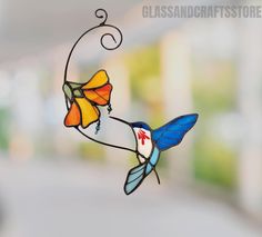 a stained glass hummingbird hanging from a wire with flowers on it's back