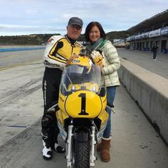 a man and woman standing next to a yellow motorcycle on the side of a road