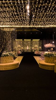 a room with lights and couches in the center, surrounded by flowers and greenery