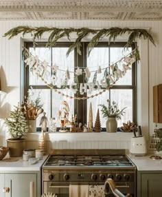 a kitchen decorated for christmas with greenery and garland hanging from the window above the stove