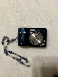 a camera is laying on top of a white blanket with a beaded necklace attached to it