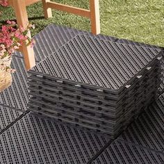 a stack of black plastic bricks sitting on top of a grass covered ground next to a wooden chair